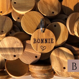 May include: A close-up of a pile of round wooden tags with a single tag engraved with the name "BONNIE" and a heart. The tags have a hole for a key ring.