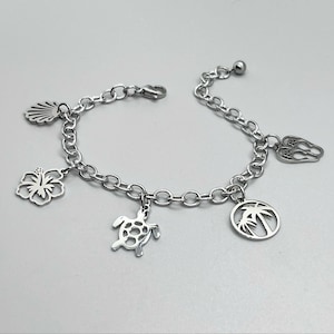 May include: Silver-toned charm bracelet featuring a seashell, hibiscus flower, turtle, palm tree, and other tropical-themed charms. The bracelet has a chain link design and a lobster clasp closure.
