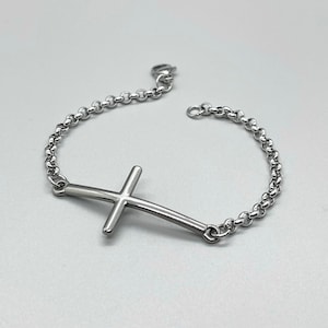 May include: A silver chain bracelet with a silver cross pendant. The cross is curved and has a simple design.