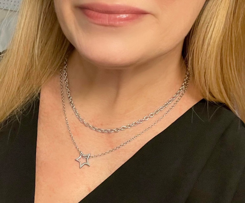 May include: A silver chain necklace with a star pendant. The necklace is layered with two chains, one thicker than the other.