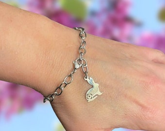 May include: A silver chain bracelet with a charm of a rabbit with a floral design.