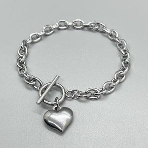 May include: A silver chain bracelet with a heart-shaped charm and a toggle clasp.