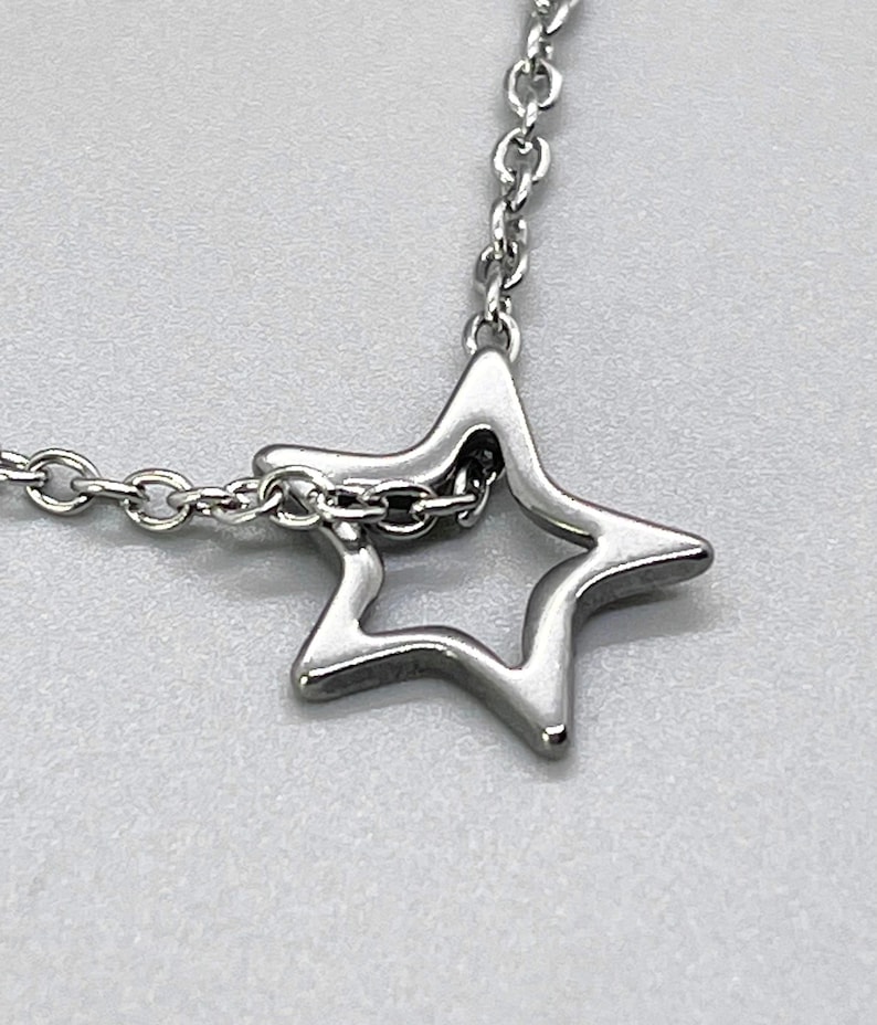 May include: A silver chain necklace with a star-shaped pendant. The star is hollow and has a delicate design.