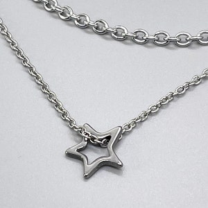 May include: A silver chain necklace with a delicate star pendant. The necklace features two chains, one thicker than the other, creating a layered look.