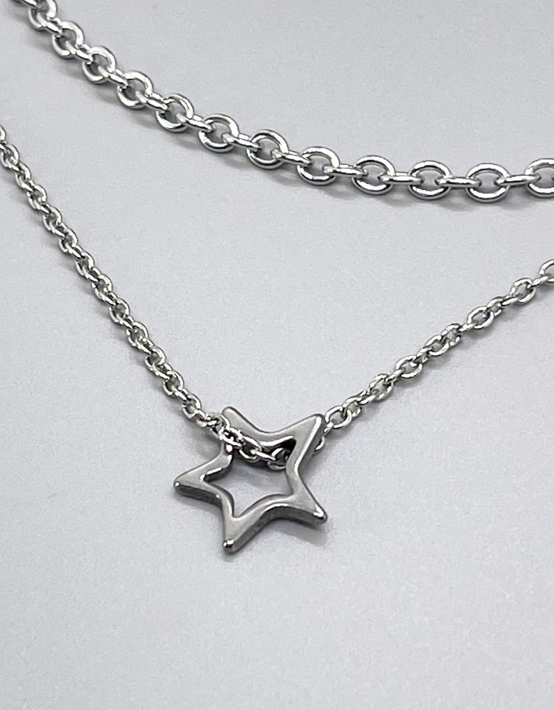 May include: A silver chain necklace with a delicate star pendant. The necklace features two chains, one thicker than the other, creating a layered look.