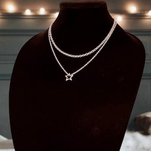 May include: A delicate gold-toned layered necklace with a star pendant. The necklace is displayed on a black velvet mannequin bust.