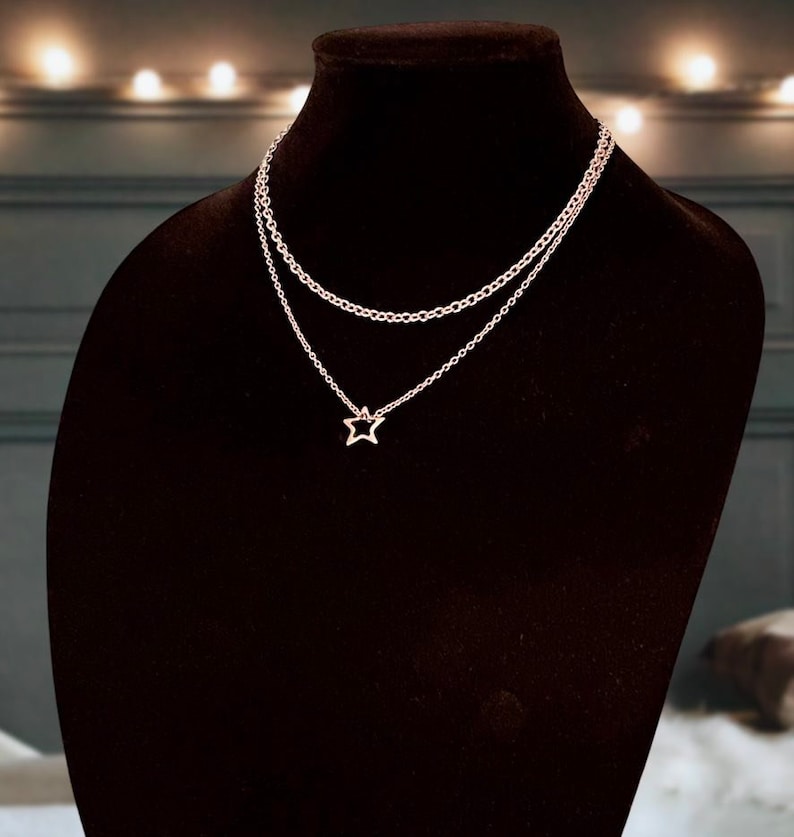 May include: A delicate gold-toned layered necklace with a star pendant. The necklace is displayed on a black velvet mannequin bust.