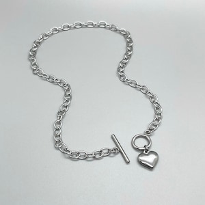 May include: A silver chain necklace with a heart-shaped pendant and a toggle clasp.