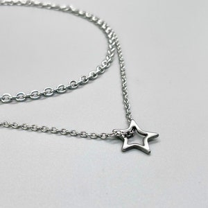 May include: A silver chain necklace with a delicate star pendant. The chain is layered, creating a stylish and modern look.