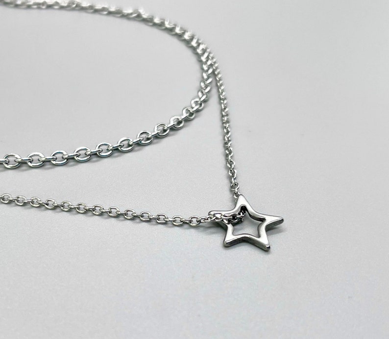 May include: A silver chain necklace with a delicate star pendant. The chain is layered, creating a stylish and modern look.