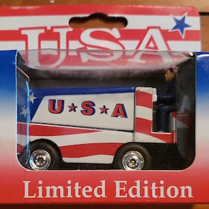May include: A red, white, and blue toy truck with a driver figure. The truck has the words "U*S*A" on the side and says "Limited Edition" on the bottom of the box.