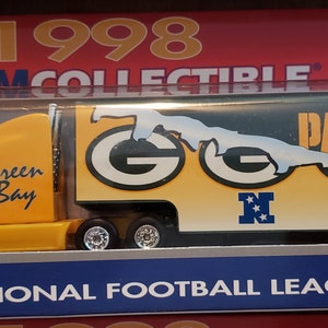 May include: A yellow 1998 Green Bay Packers Team Collectible semi-truck toy with a green and yellow trailer. The trailer has the words "Packers" and "Green Bay" on it. The toy is in a box with the words "National Football League" on it.
