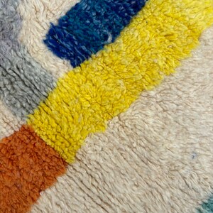 May include: Close-up of a colorful, woven rug with stripes of yellow, blue, orange, and gray.