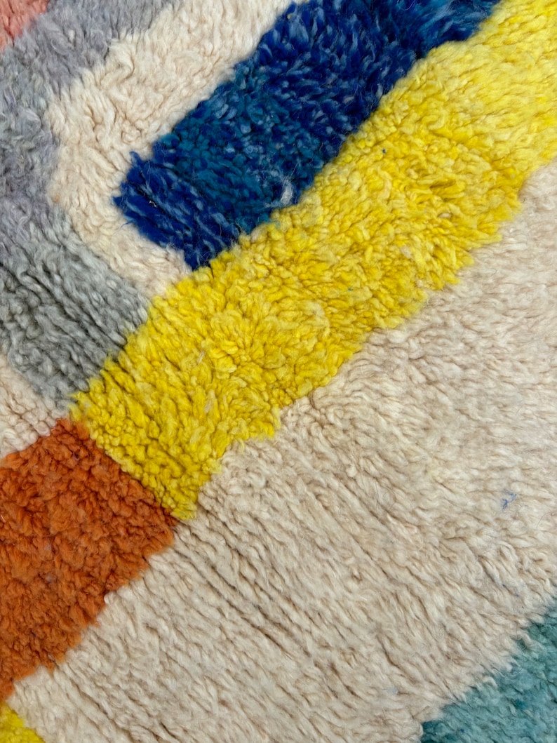 May include: Close-up of a colorful, woven rug with stripes of yellow, blue, orange, and gray.