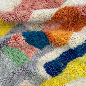 May include: A colorful, geometric patterned rug with a soft, fluffy texture. The rug features shades of pink, orange, yellow, blue, green, and gray.
