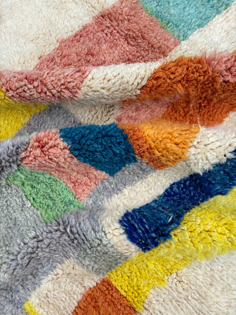 May include: A colorful, geometric patterned rug with a soft, fluffy texture. The rug features shades of pink, orange, yellow, blue, green, and gray.