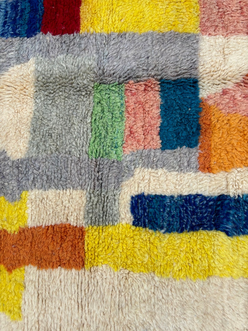 May include: A colorful, geometric rug with a variety of textures. The rug features squares and rectangles in shades of blue, red, yellow, green, orange, and white.