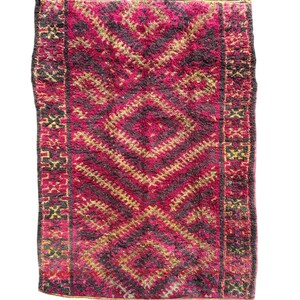 May include: A rectangular rug with a central diamond pattern in shades of fuchsia, black, and gold. The rug has a textured, woven appearance with a border featuring geometric designs. The rug is suitable for home decor.