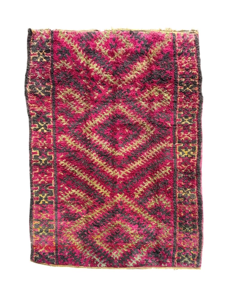 May include: A rectangular rug with a central diamond pattern in shades of fuchsia, black, and gold. The rug has a textured, woven appearance with a border featuring geometric designs. The rug is suitable for home decor.
