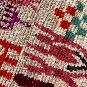 May include: Close-up of a colourful woven rug with a geometric pattern. The rug is made of wool and has a variety of colours, including red, orange, green, and purple.