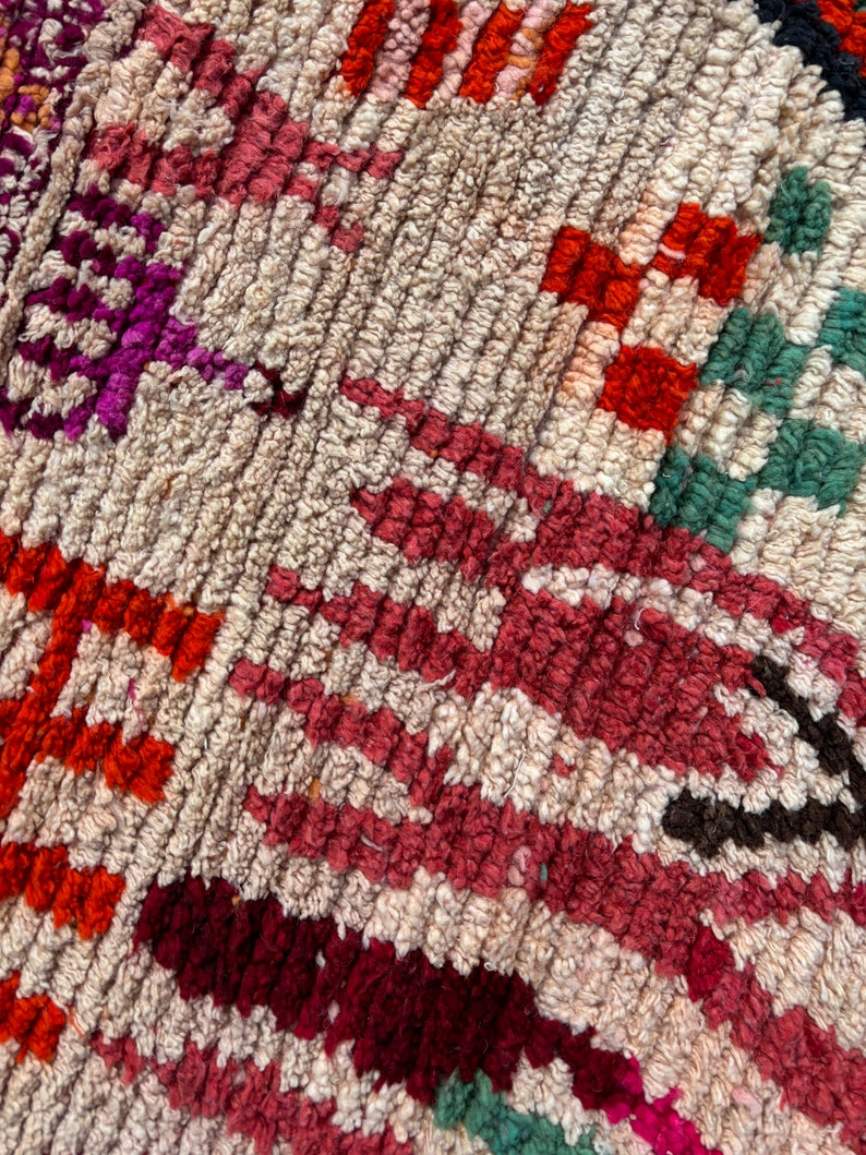 May include: Close-up of a colourful woven rug with a geometric pattern. The rug is made of wool and has a variety of colours, including red, orange, green, and purple.