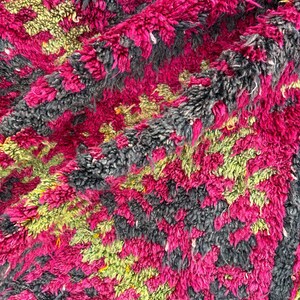 May include: A close-up of a plush, textured rug with a vibrant color palette. The rug features a pattern of magenta, gray, and lime green. The thick pile creates a soft, inviting appearance, suitable for a living room or bedroom.