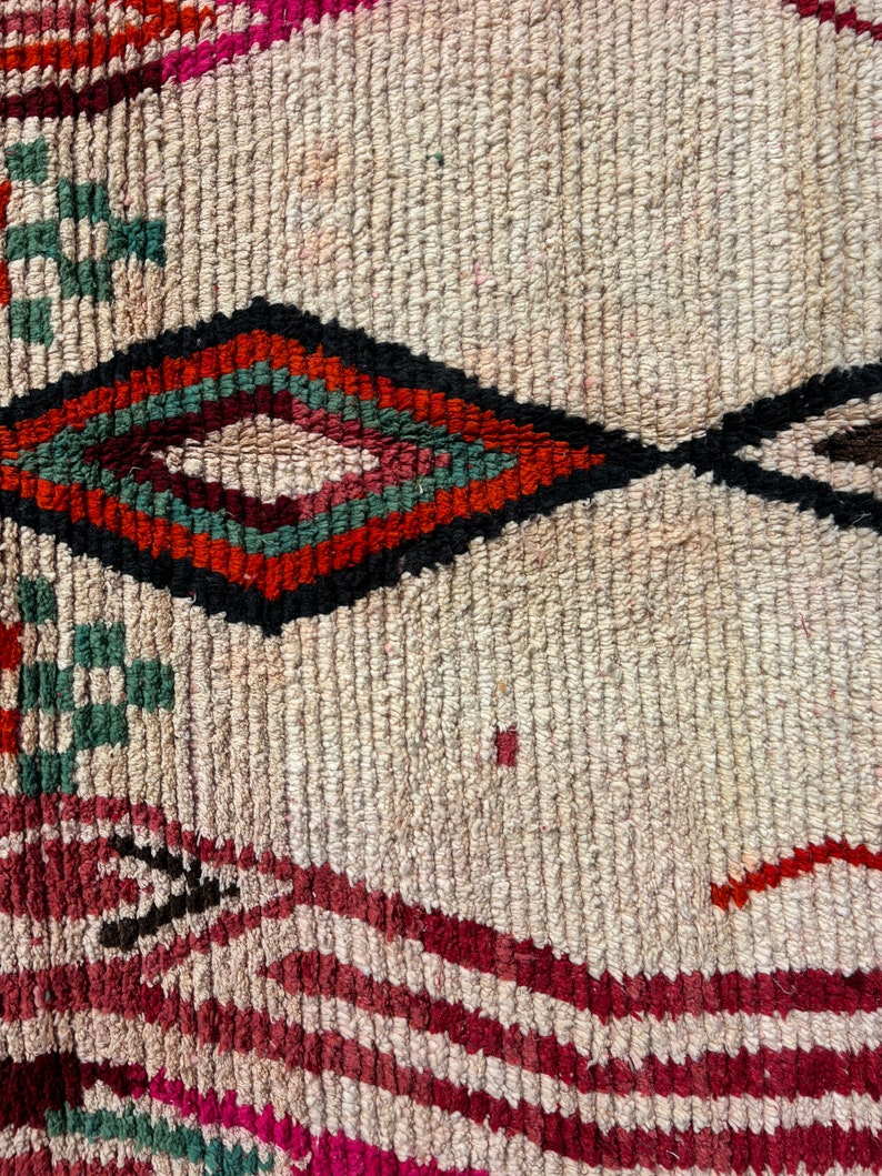 May include: Close-up of a woven rug with a diamond pattern in shades of red, green, and black on a cream background.