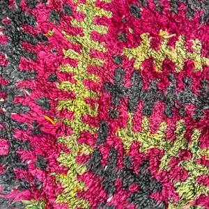 May include: Close-up of a textured rug with a pattern of magenta, lime green, and charcoal gray. The rug's design features a repeating geometric pattern, creating a visually interesting and tactile surface. The rug is made of a soft, plush material.