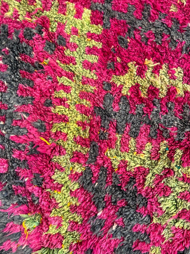 May include: Close-up of a textured rug with a pattern of magenta, lime green, and charcoal gray. The rug's design features a repeating geometric pattern, creating a visually interesting and tactile surface. The rug is made of a soft, plush material.