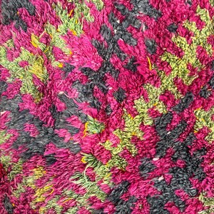 May include: Close-up of a textured rug with a vibrant pattern. The rug features a mix of colors, including hot pink, black, and green, creating a visually dynamic design. The texture appears soft and plush.