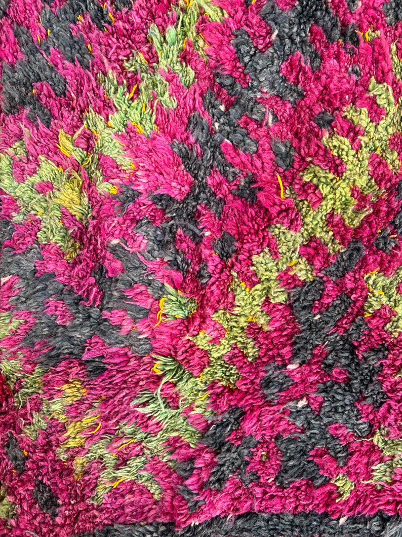 May include: Close-up of a textured rug with a vibrant pattern. The rug features a mix of colors, including hot pink, black, and green, creating a visually dynamic design. The texture appears soft and plush.