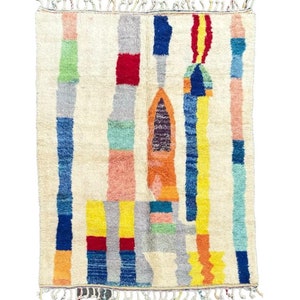 May include: A colorful Moroccan rug with a geometric design featuring a variety of colors including red, blue, yellow, green, and orange. The rug has a white background and a fringe border.