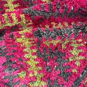 May include: Close-up of a plush, textured rug with a vibrant color palette. The rug features a pattern of magenta, gray, and lime green hues. The thick pile suggests a soft and comfortable texture, ideal for home decor.