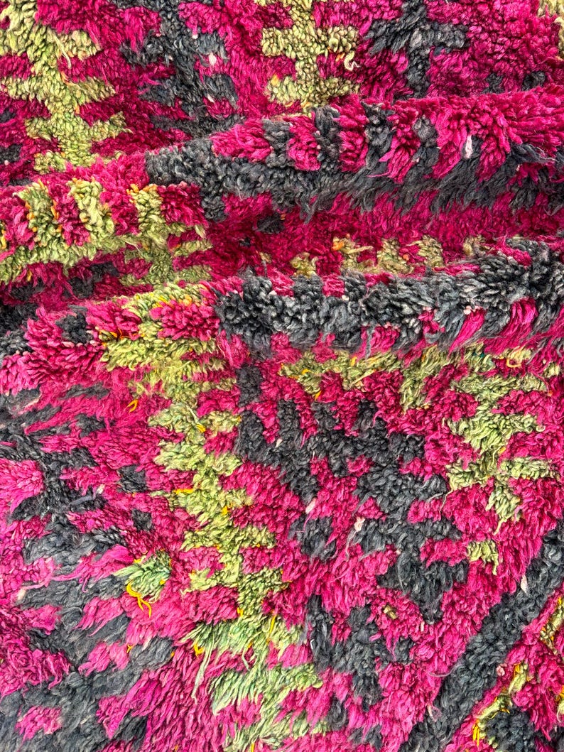 May include: Close-up of a plush, textured rug with a vibrant color palette. The rug features a pattern of magenta, gray, and lime green hues. The thick pile suggests a soft and comfortable texture, ideal for home decor.