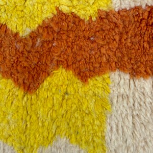 May include: Close-up of a textured rug with a geometric pattern in shades of yellow, orange, and white.