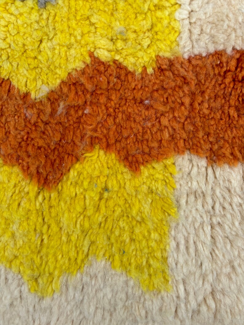 May include: Close-up of a textured rug with a geometric pattern in shades of yellow, orange, and white.