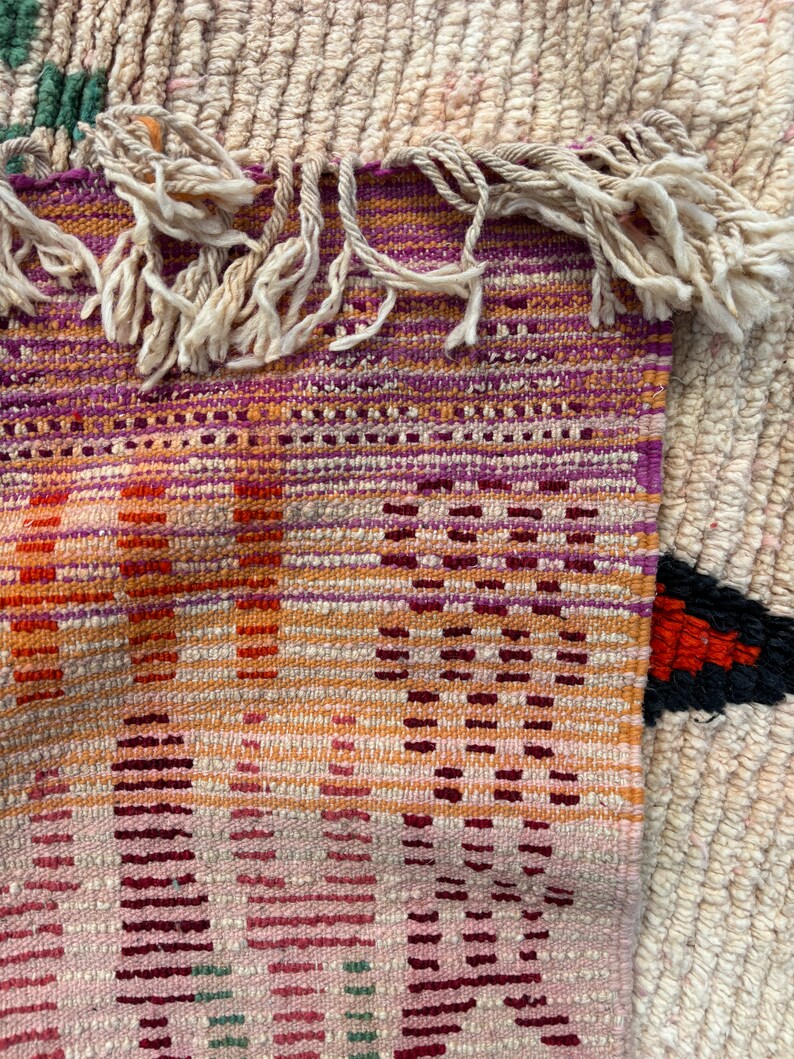 May include: A close-up of a woven rug with a colourful geometric pattern. The rug has a fringe border and is made of natural fibres.