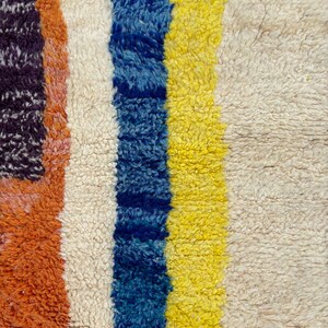 May include: Close-up of a colorful striped rug with a white, blue, yellow, and orange pattern. The rug is made of a soft, fluffy material.