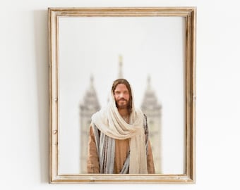 May include: A framed watercolour painting of a man with long brown hair and a beard wearing a white robe and standing in front of a blurry background of a building.