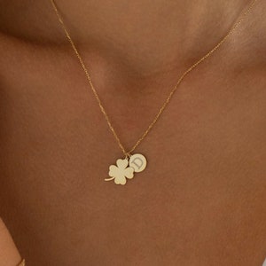 May include: A gold necklace with a four-leaf clover charm and a small round charm with the letter D engraved on it.