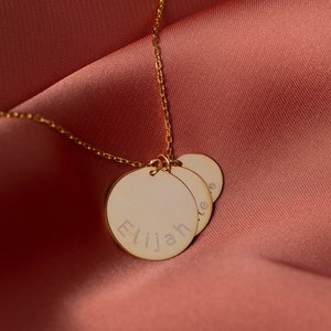 May include: Gold necklace with three round pendants, the largest pendant is engraved with the name "Elijah".