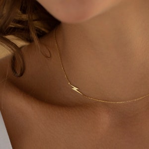 May include: A gold necklace with a lightning bolt pendant. The necklace is delicate and simple, making it a perfect everyday piece of jewelry.