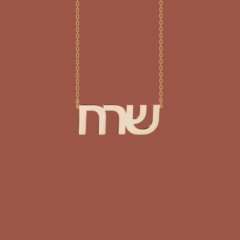 May include: A gold necklace with a pendant featuring the Hebrew letters "mey" which means "water" in Hebrew.