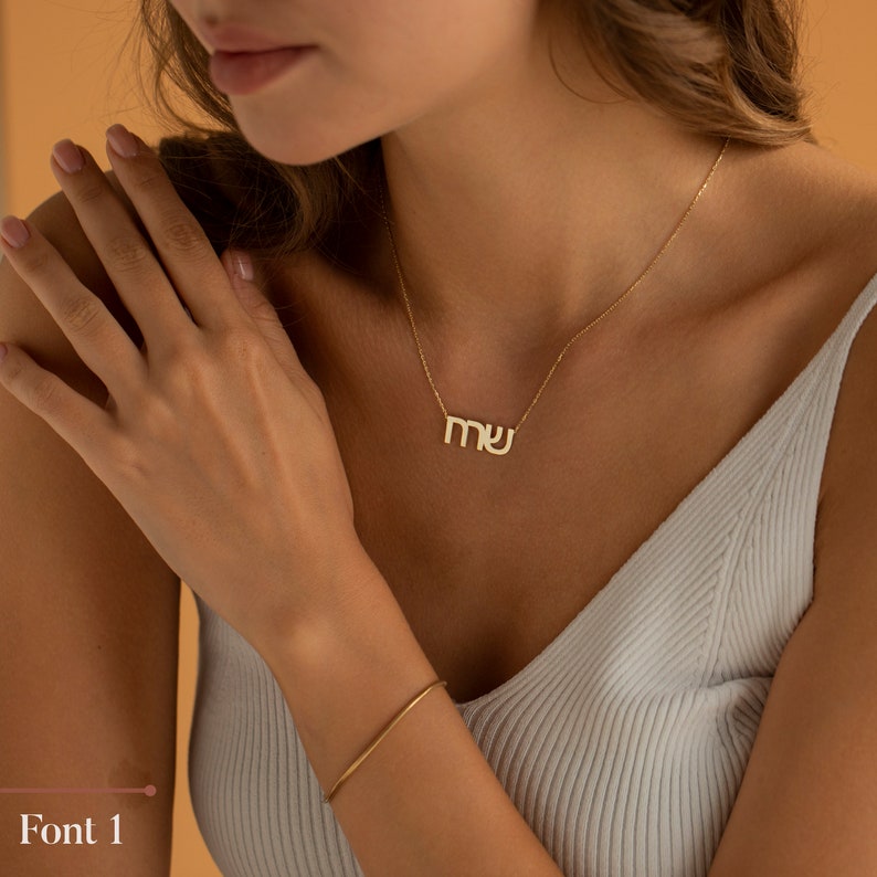 May include: A gold necklace with a delicate chain and a pendant with the letters "MU" in a simple, modern font.