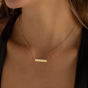 May include: A gold chain necklace with a thin, rectangular pendant.