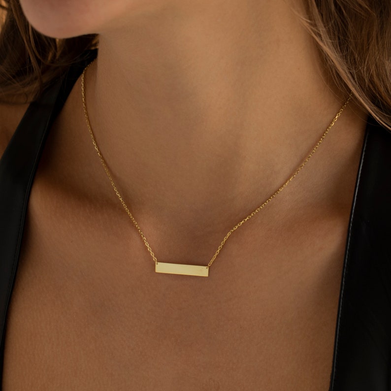 May include: A gold chain necklace with a thin, rectangular pendant.