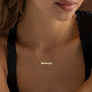 May include: A gold necklace with a thin chain and a rectangular pendant engraved with the coordinates "37.33 N 81.2844 W".