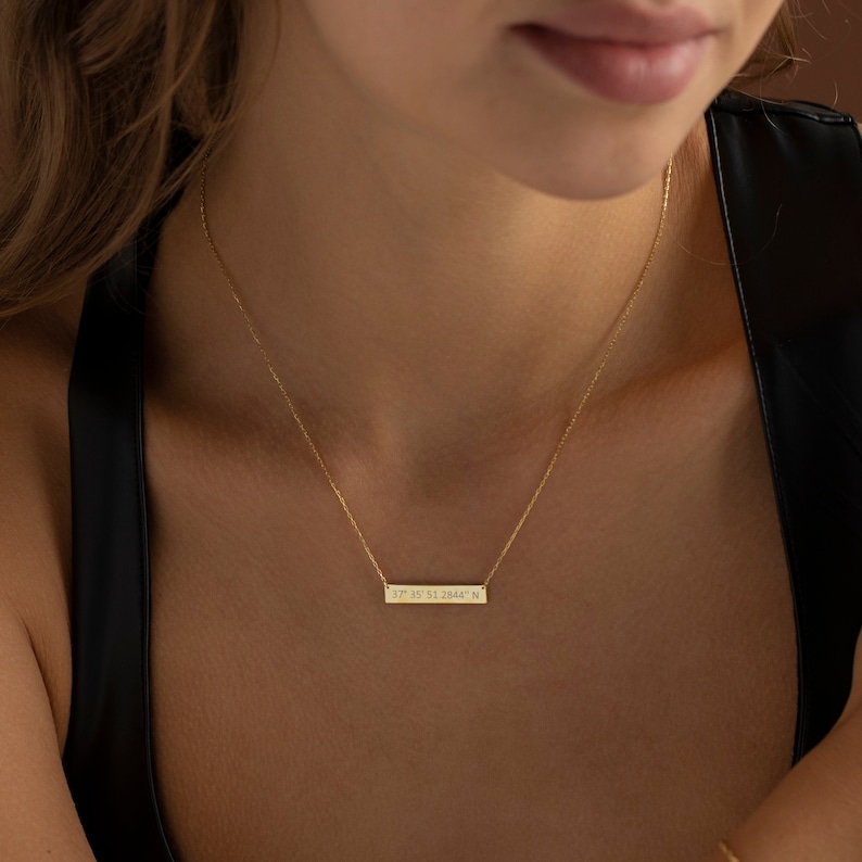 May include: A gold necklace with a thin chain and a rectangular pendant engraved with the coordinates "37.33 N 81.2844 W".