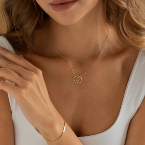 Puede incluir: Un collar de oro con un delicado colgante de mano de Hamsa. El colgante es un c&iacute;rculo con un dise&ntilde;o calado de una mano de Hamsa.