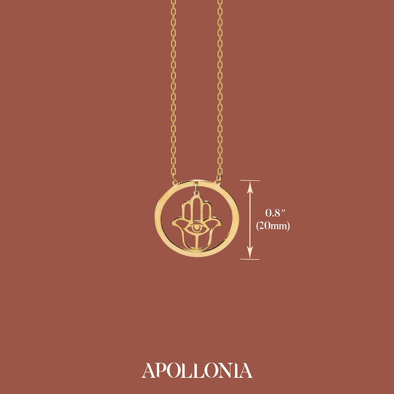 Puede incluir: Collar de oro con un dije de mano de hamsa con un ojo en el centro. El dije tiene un di&aacute;metro de 20 mm.